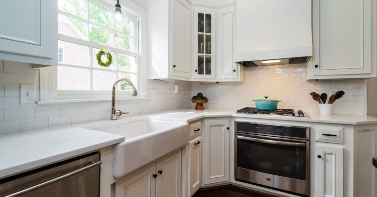 A modern farmhouse kitchen with a white farmhouse ceramic sink with a stainless steel faucet under a window.