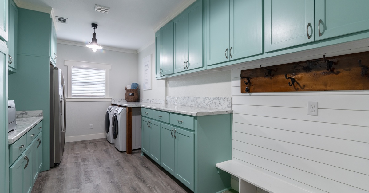 A mudroom and laundry room with a refrigerator. The cabinets are mint green with a white bench and a washer and dryer.