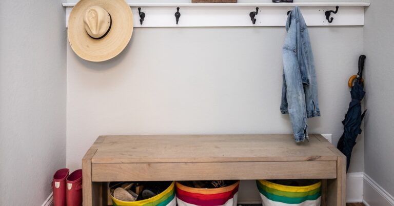 A home's mudroom with a wooden bench and hooks mounted on the wall. On the hooks are a beach hat and a denim jacket.