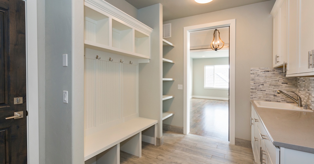 A mudroom entryway to a home with a built-in bench, hooks on the walls, and cabinets. There's also a kitchenette.