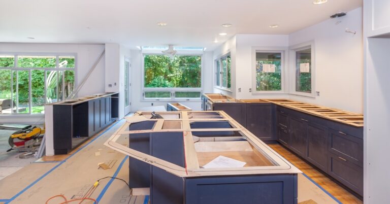 A home's kitchen in the middle of a remodel with blue cabinetry without countertops and covered floors.