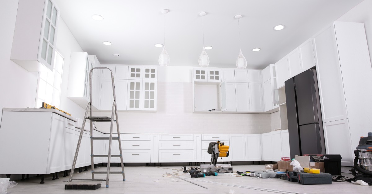 A low view of a kitchen with white cabinets and countertops with various tools and maintenance equipment on the floor.