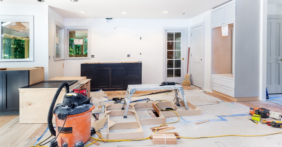 A home kitchen in the middle of a remodel with empty walls, unpainted cabinetry on the floor, and various tools.