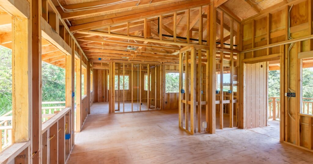 The interior of a new home under construction with empty windows and door frames and wooden studs for walls.
