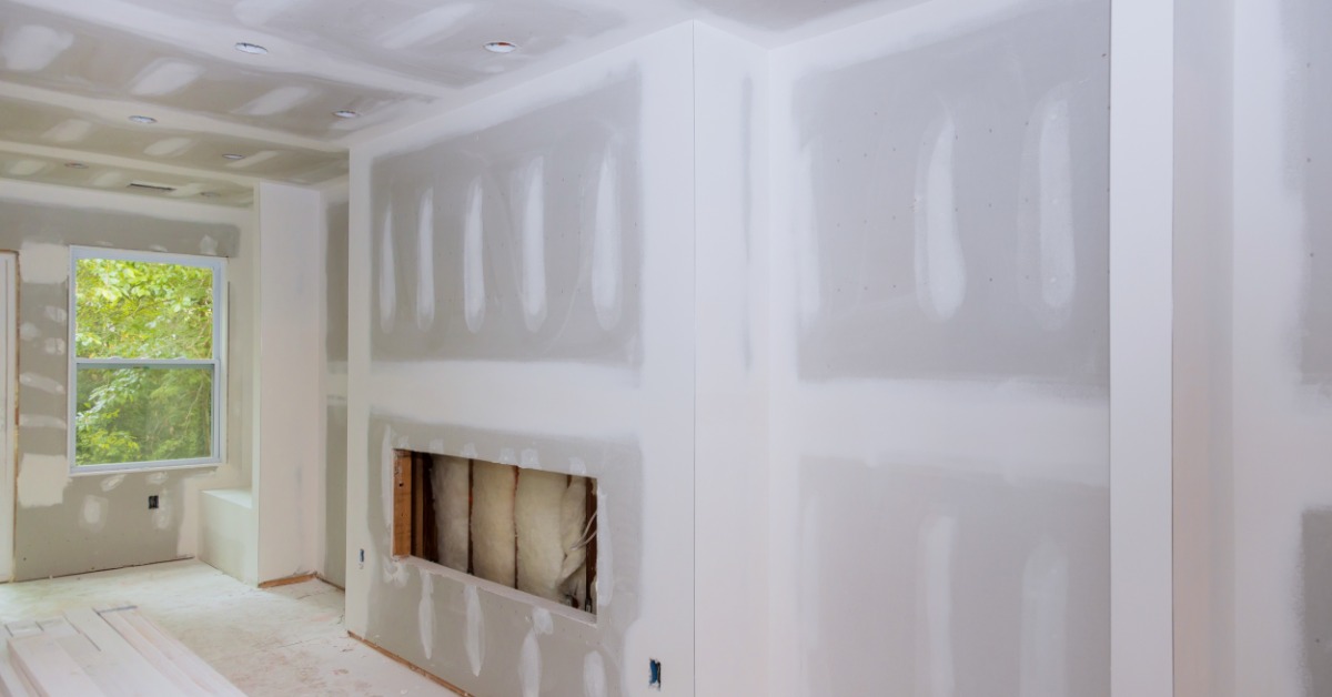An upper level of a home under renovation with drywall finishing and a make-shift workbench in the middle of the room.