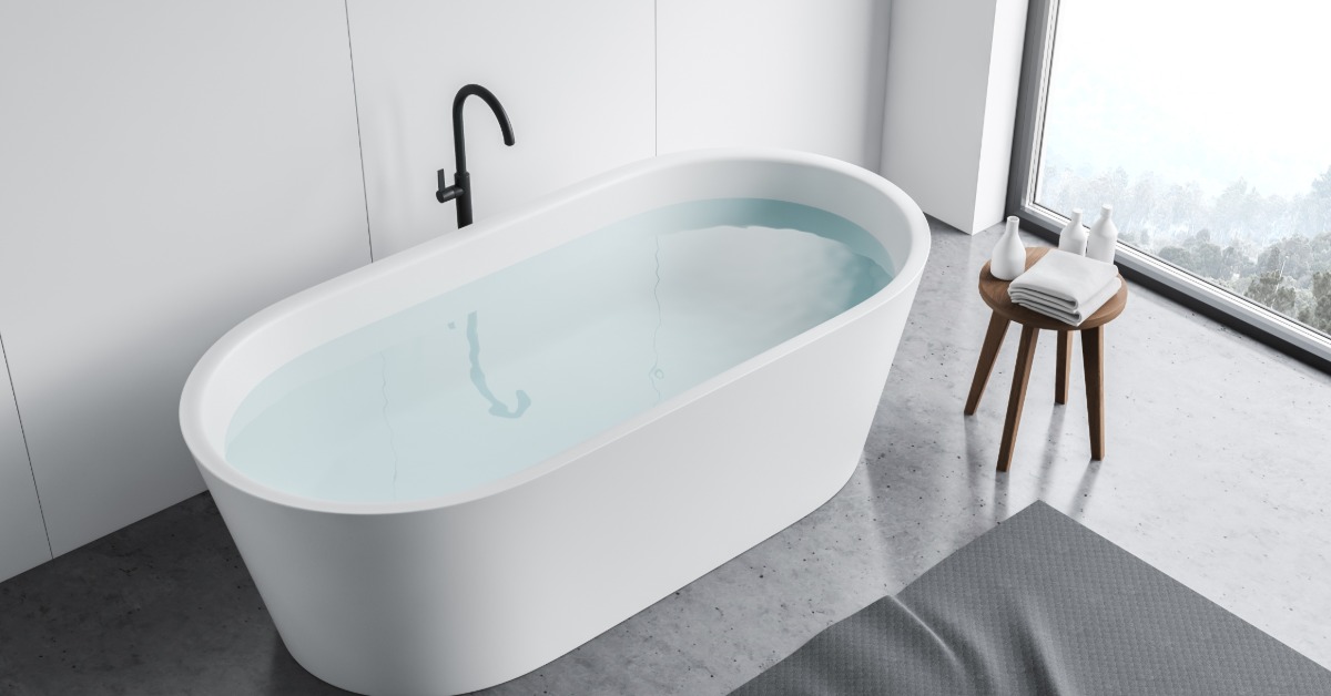 An elevated view looking down of a modern bathroom with a concrete floor and a white modern bathtub next to a window.