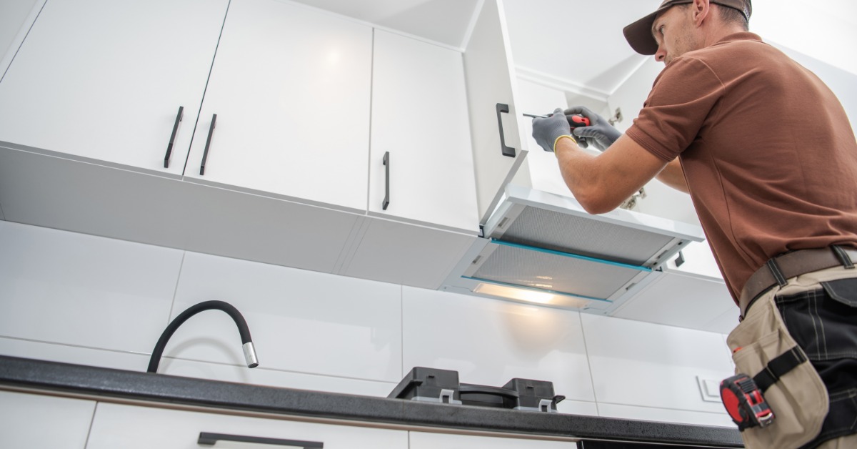A ground-level view looking up at a man with a screwdriver installing handles onto white cabinets in a kitchen.