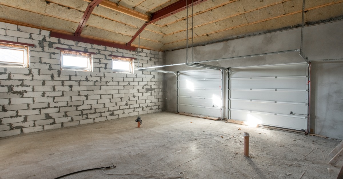 A large, two-stall garage with white doors and three windows that's been stripped bare for construction.