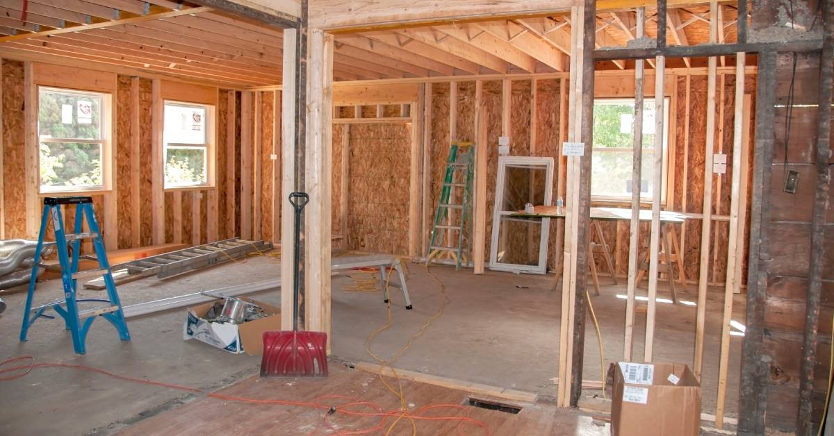 A view from inside a home addition project in the middle of construction with bare walls, wooden studs, and work equipment.