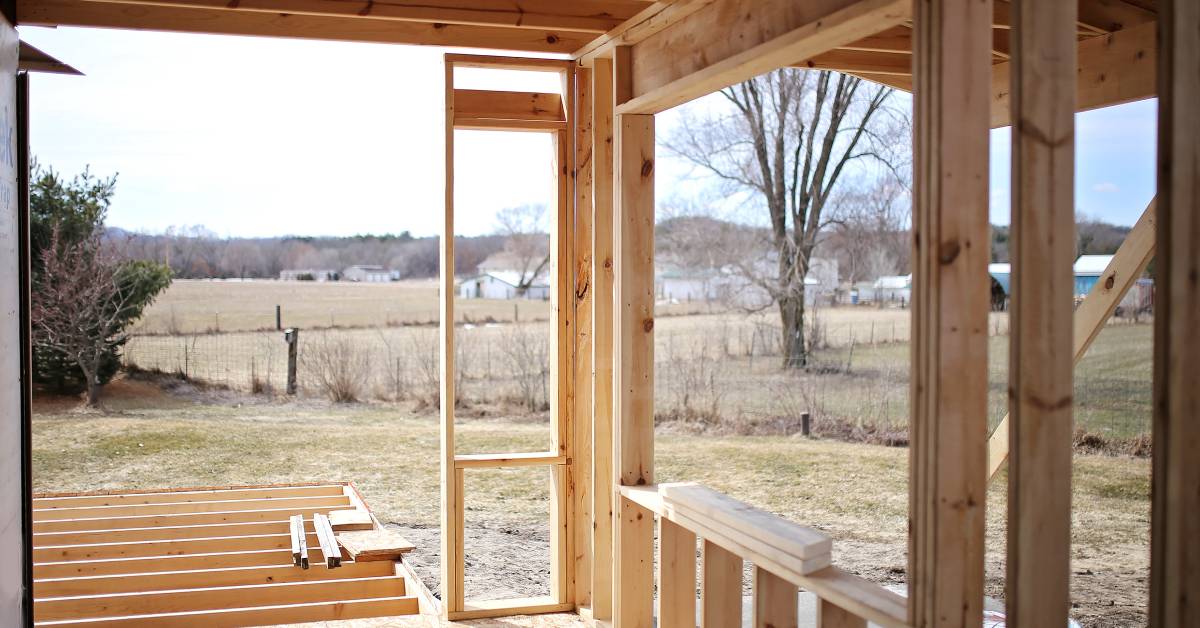 A view from within the unfinished framing of a home addition for a house, looking out into fields behind the home.
