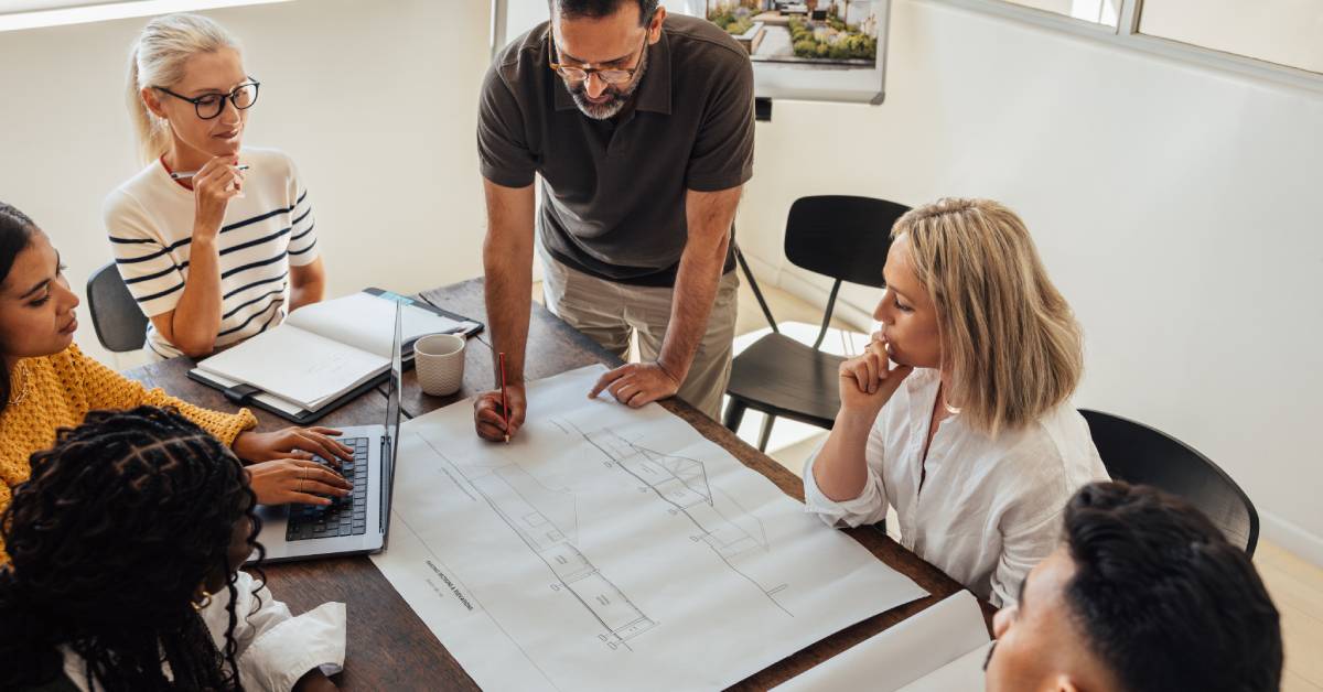 A group of professionals sitting around a meeting table examining blueprints for a new home design in a conference room.