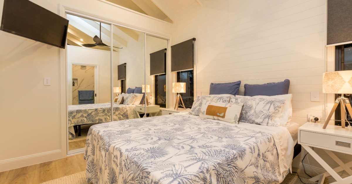 The bedroom inside an in-law suite has a bed, a closet, a mirror, a mounted television, and a ceiling fan.