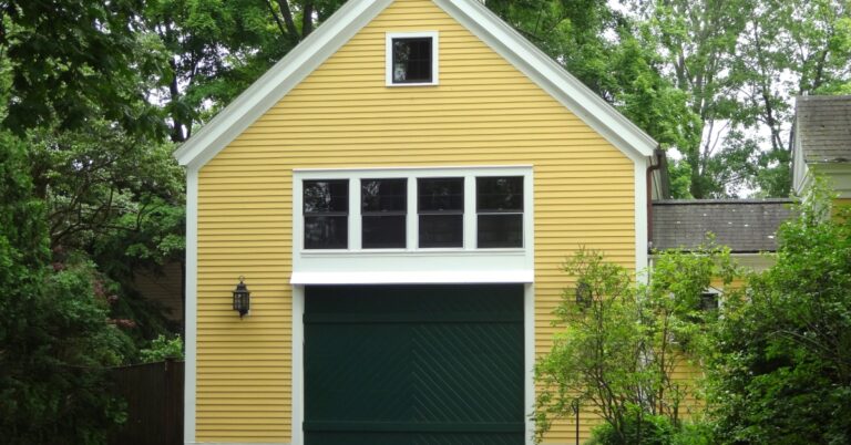 The exterior of a yellow bonus room addition above a garage connected to a home with trees surrounding the outside.