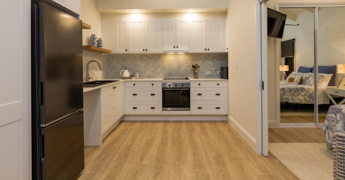 A connected kitchen of an in-law suite with white cabinetry and a sliding door that connects to a bedroom.
