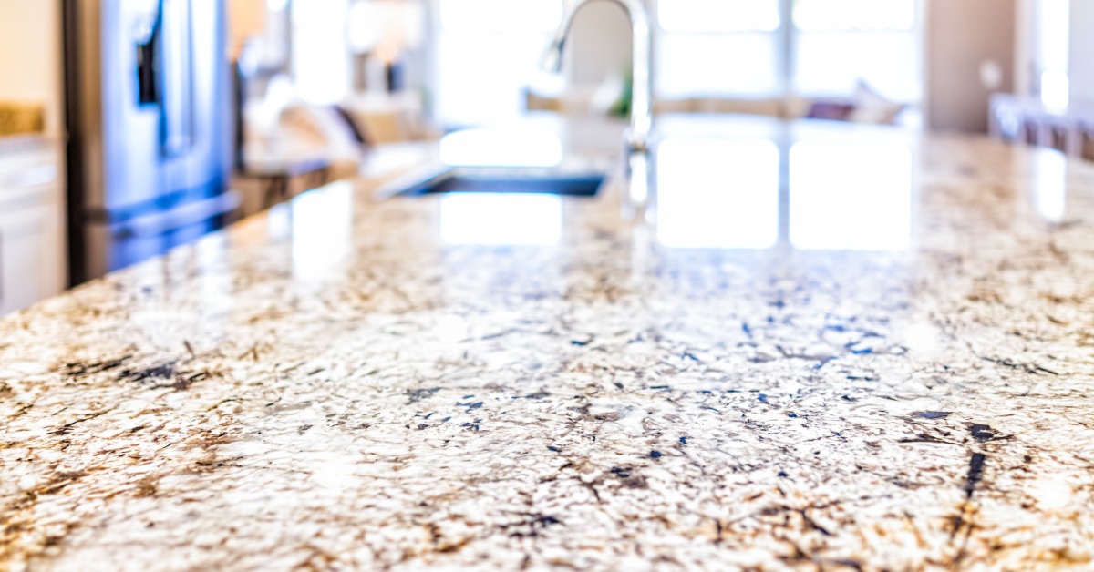 A close-up of a granite countertop in a modern kitchen with daylight from the windows reflecting off the surface.
