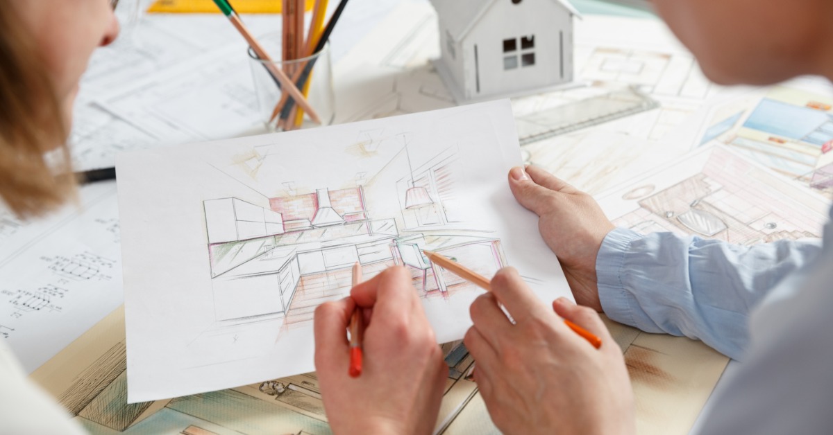 An over-the-shoulder view of a man and a woman looking at a sketch of a home kitchen with pencils on a desk.