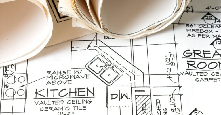 A close-up of the design and layout plans for a new home, with a focus on the kitchen, next to rolled-up papers.