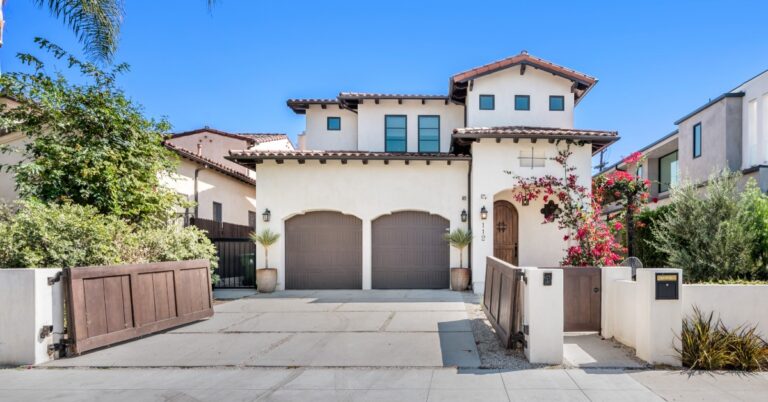 A view from the street of a two-story, Spanish-style home with a clay-tile roof, a two-stall garage, and a gate.