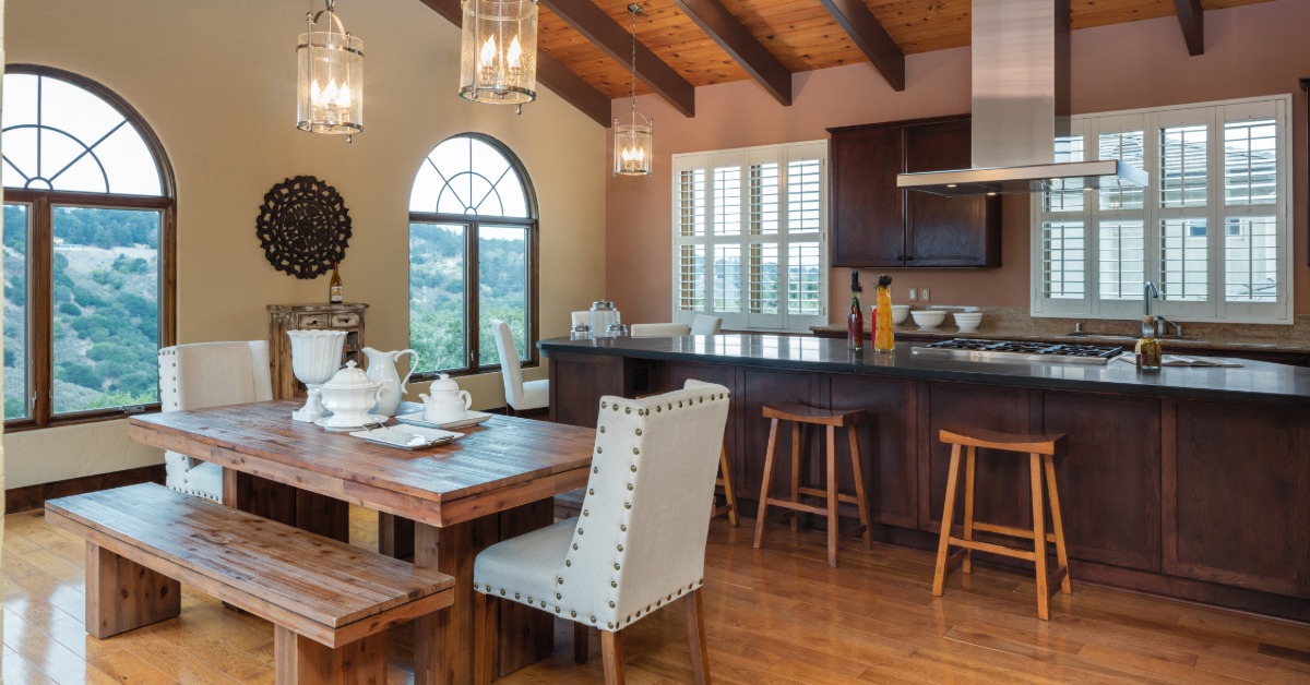 The interior o a Mediterranean-style home with an open-floor plan, dark wood cabinets, and a wooden dining table and bench.