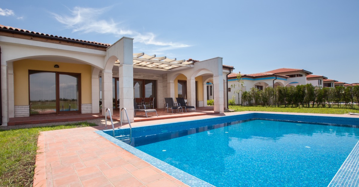 The backyard of a Mediterranean-style home with a pool, a red-tile patio, a pergola, and rounded arches.