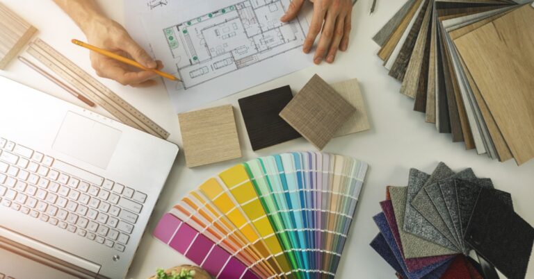 An overhead view of a desk with color samples, flooring material samples, a laptop, and interior design schematics.