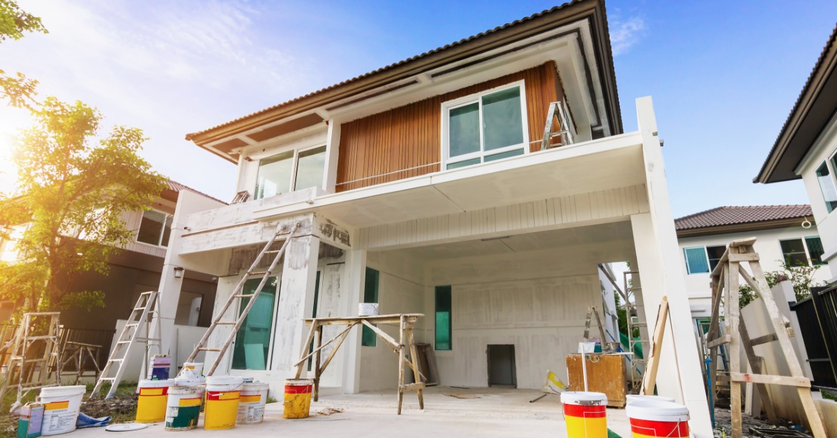 A view from the driveway of a two-story home under construction and painting with various buckets and ladders around.