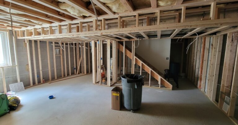 A residential basement partially finished. The floor is uncovered concrete, and the walls are bare, with only the studs.