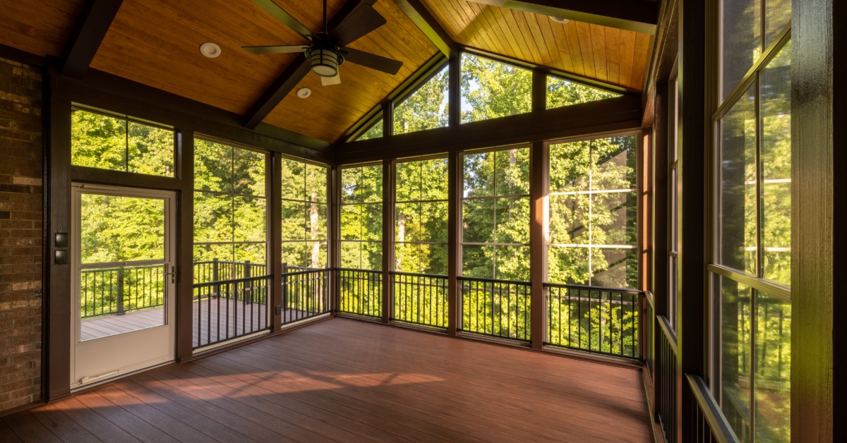 A view from inside looking out at a modern screen porch with plastic windows and a composite floor with a forest outside.