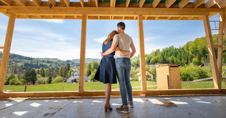 A rear view of a man and woman standing together on the first floor of an unfinished home, looking at a green valley.