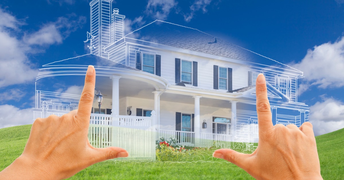 A point-of-view of two hands framing a transparent gradient sketch of a multi-story home over a bare stretch of grassy land.