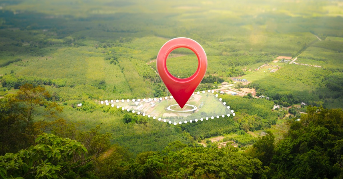 An aerial, landscape view of valley land with a transparent outline over a plot and a giant red pin over it.