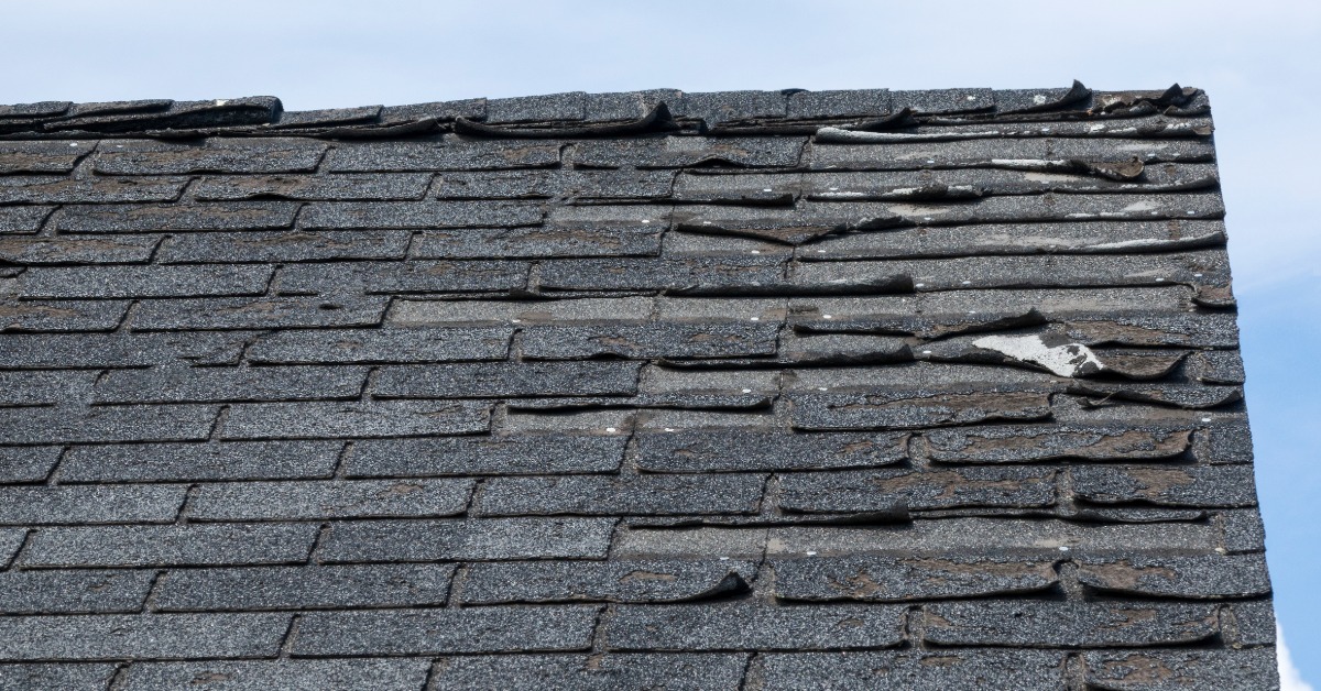A close-up of the roof of a home with damage. The shingled roof features damaged and missing shingles.