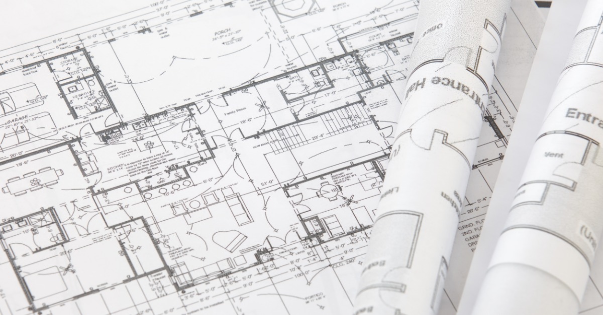 A close-up of a large architectural floor plan with technical drawings and two other architectural rolls on top of it.
