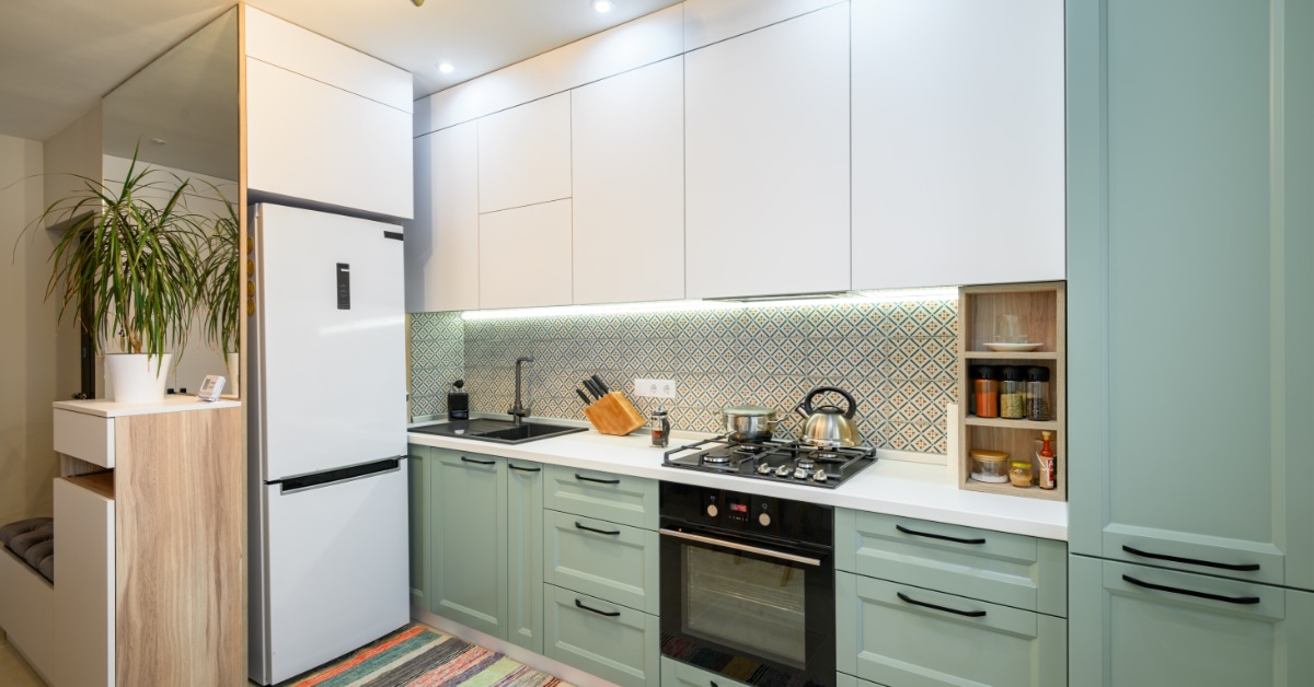 A small, modern kitchen in a home with teal cabinetry, a diamond-style backsplash, a gas stovetop, and a fridge.