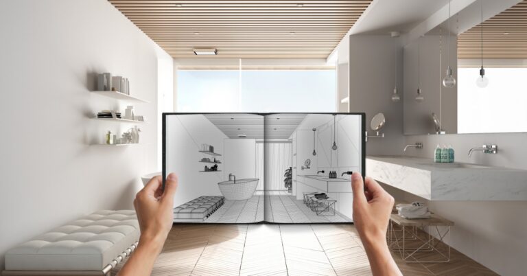 A point of view of a pair of hands holding up a notebook with a sketch of a bathroom design in front of a bathroom.