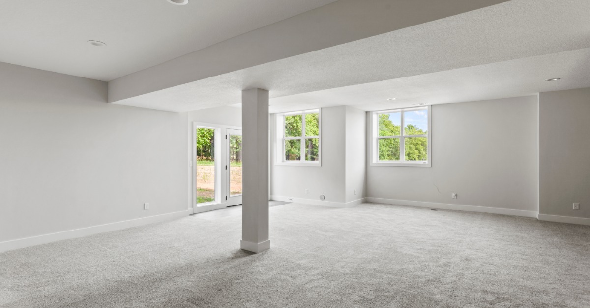 The finished basement of a home with grey carpeting, a structural column in the middle, and sliding doors leading outside.
