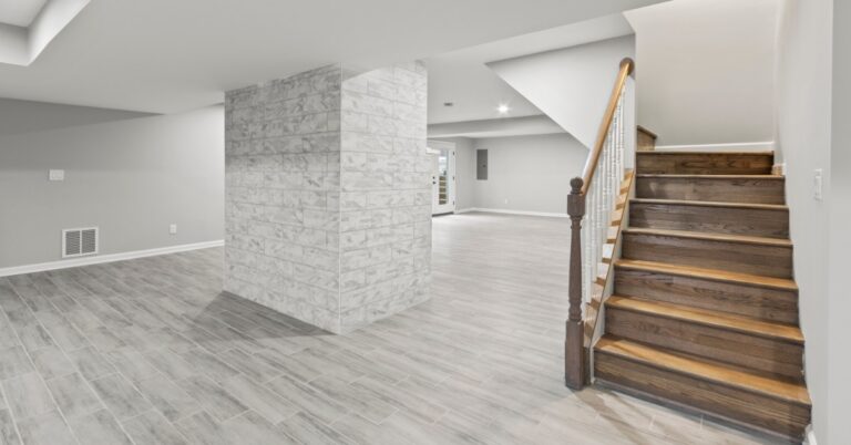 The finished basement of a home with a wooden staircase and a large, stone pillar structural column in the middle.