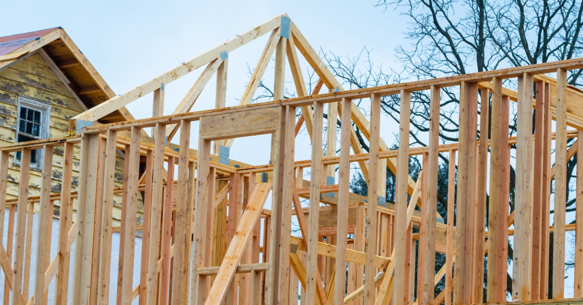 A view from below of the wooden frame of a second-story addition to a house on a cloudy day with trees behind it.