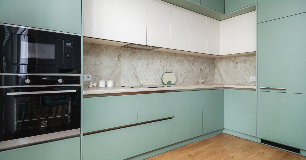 A modern home kitchen with teal and white cabinetry with flat-panel door style and stone countertops and backsplash.