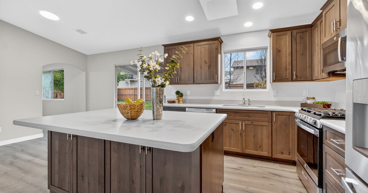 A modern home kitchen with an island featuring white stone countertops and brown cabinetry with shaker-style doors.