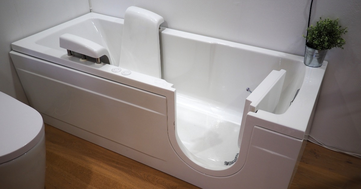A close-up of a handicap-accessible bathtub in a modern home with wood flooring. The tub features a door and handles.