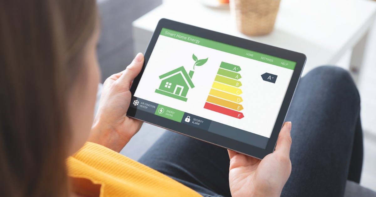 An over-the-shoulder view of a woman looking at a digital tablet showing smart home energy statistics.